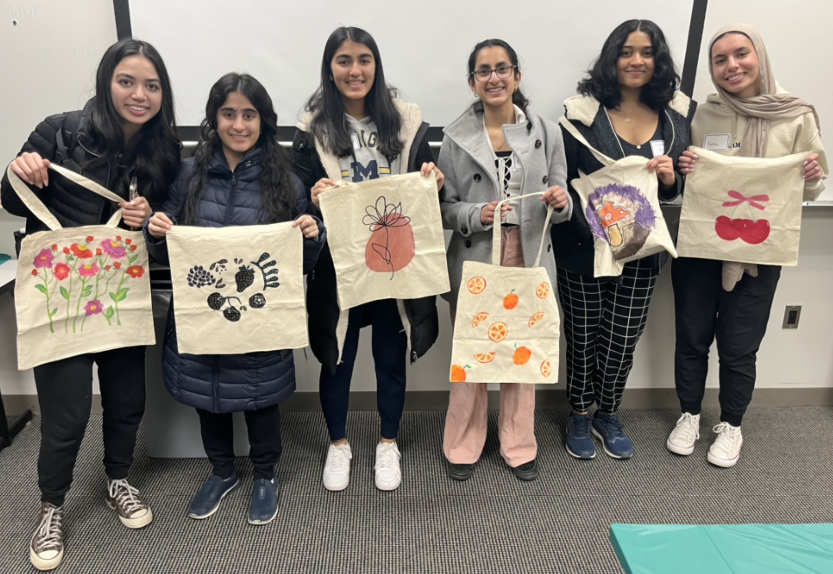 Six WISE students stand together holding up hand painted tote bags made at a WISE Night In Event.